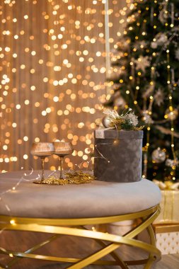 Güzel dekore edilmiş bir Noel ağacı, hediye kutularıyla çevrili, şampanya bardaklı şık bir masanın yanında duruyor, sıcak sicim ışıklarının zeminine kurulmuş, büyülü şenlik atmosferi