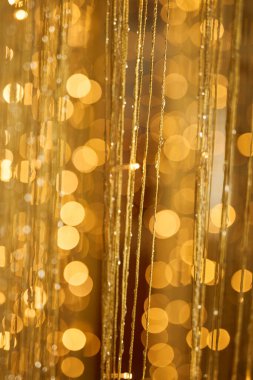 Ilık altın bokeh ışıkları ve narin parıldayan ipliklerle dolu ışıl ışıl bir arka plan, kutlama ve lüks temalar için uygun şenlikli, zarif ve soyut bir aydınlatma efekti yaratıyor.