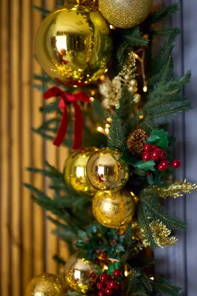 Parlak altın takılar, kırmızı böğürtlenler ve doğal çam kozalaklarıyla süslenmiş, ışıldayan ışıklarla sarmalanmış, zengin ve zengin bir Noel süsü oluşturan bir Noel çelengi.