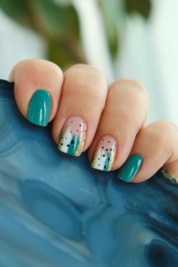 Modern deniz mavisi ve soyut tırnak sanatı manikürüne sahip bir kadın eli, doğal ve şık elementler arasındaki zıtlığı vurgulamak için kaba, karanlık bir taş tutuyor.