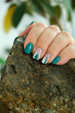 Modern deniz mavisi ve soyut tırnak sanatı manikürüne sahip bir kadın eli, doğal ve şık elementler arasındaki zıtlığı vurgulamak için kaba, karanlık bir taş tutuyor.