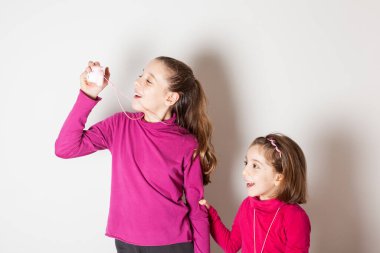 Beyaz arka planda oyuncak fotoğraf makinesiyle fotoğraf çeken iki küçük kız.