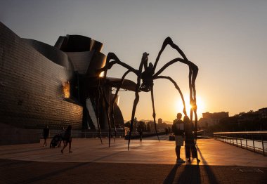 Bilbao, İspanya - 02 Ağustos 2022: Louise Bourgeois 'in günbatımında Guggenheim Müzesi' nin yanındaki Mamam adlı Örümcek heykeli