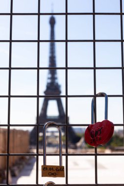 Demir ızgaraya kırmızı aşk kilidi, iki sevgili ismi ve arka planda Eyfel Kulesi, Paris