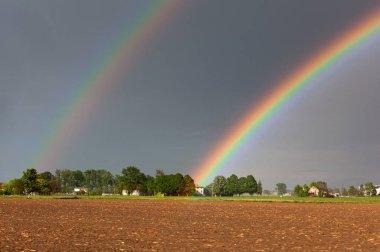 Kırsal bir çiftliğin üzerinde, tehlikeli ve fırtınalı bir gökyüzünün arka planında güzel, renkli bir gökkuşağı.