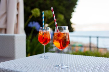 Bir yaz akşamı plaj kenarındaki bir barda beyaz bir masada pipetle iki aperol spreyi.