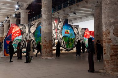 Venice, Italy - April 17, 2024: Visitors of the 60th International Art exhibition of Venice biennale titled Foreigners Everywhere, Stranieri Ovunque. On background the Artwork by Frieda Toranzo Jaeger, titled Rage is a machine in times of senselessne clipart