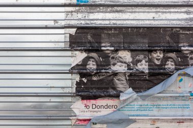 Milan, İtalya - 16 Mart 2024: Siyah-beyaz çocukların resimlerinin olduğu yırtık eski poster, panjura yapışmış