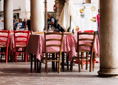 Mantova, İtalya - 15 Eylül 2024: Şehrin ikonik portikolarının altındaki bir restoranın önünde boş masa ve sandalyeler, klasik İtalyan kırmızı ve beyaz kareli masa örtülerinin yer aldığı masalar