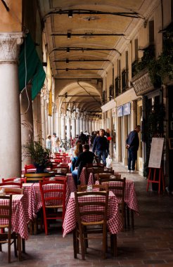 Mantova, İtalya - 15 Eylül 2024: Şehrin ikonik portikolarının altındaki bir restoranın önünde boş masa ve sandalyeler, klasik İtalyan kırmızı ve beyaz kareli masa örtülerinin yer aldığı masalar