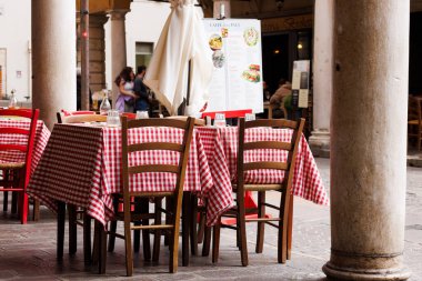 Mantova, İtalya - 15 Eylül 2024: Şehrin ikonik portikolarının altındaki bir restoranın önünde boş masa ve sandalyeler, klasik İtalyan kırmızı ve beyaz kareli masa örtülerinin yer aldığı masalar