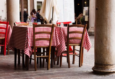 Şehrin ikonik kapılarının altındaki bir restoranın dışındaki boş masa ve sandalyelerde klasik İtalyan kırmızı ve beyaz kareli masa örtüleri, Mantua