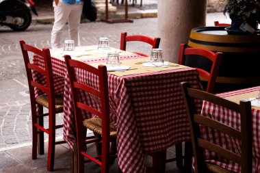 Şehrin ikonik kapılarının altındaki bir restoranın dışındaki boş masa ve sandalyelerde klasik İtalyan kırmızı ve beyaz kareli masa örtüleri, Mantua