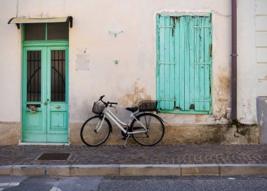 Vintage-style bicycle leaning against the textured wall of an Italian house, with green wooden door and shutters, capturing a classic and nostalgic Italian scene clipart