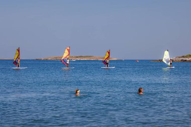 Premantura, Hırvatistan - 22 Ağustos 2024: Hırvatistan 'ın Istria kenti Premantura yakınlarındaki Cape Kamenjak' ta rüzgar sörfü okuluna giden üç erkek. Sahne, kristal berraklığında Adriyatik Denizi 'nde bir açık hava eğitim oturumunu çekiyor