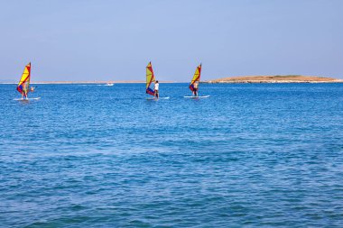 Premantura, Hırvatistan - 22 Ağustos 2024: Hırvatistan 'ın Istria kenti Premantura yakınlarındaki Cape Kamenjak' ta rüzgar sörfü okuluna giden üç erkek. Sahne, kristal berraklığında Adriyatik Denizi 'nde bir açık hava eğitim oturumunu çekiyor