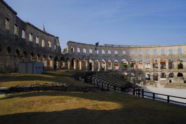 Hırvatistan 'ın Pula kentindeki antik miras. Antik Roma arenasının kemerleri. Tarihi amfi tiyatronun ayrıntıları, mavi arka plandaki yüksek duvarların geniş açılı görüntüsü..