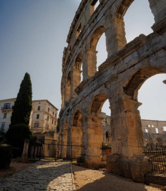 Hırvatistan 'ın Pula kentindeki antik miras. Antik Roma arenasının kemerleri. Tarihi amfi tiyatronun ayrıntıları, mavi arka plandaki yüksek duvarların geniş açılı görüntüsü..
