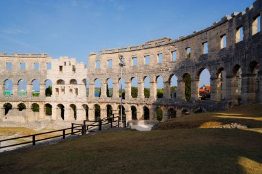 Hırvatistan 'ın Pula kentindeki antik miras. Antik Roma arenasının kemerleri. Tarihi amfi tiyatronun ayrıntıları, mavi arka plandaki yüksek duvarların geniş açılı görüntüsü..