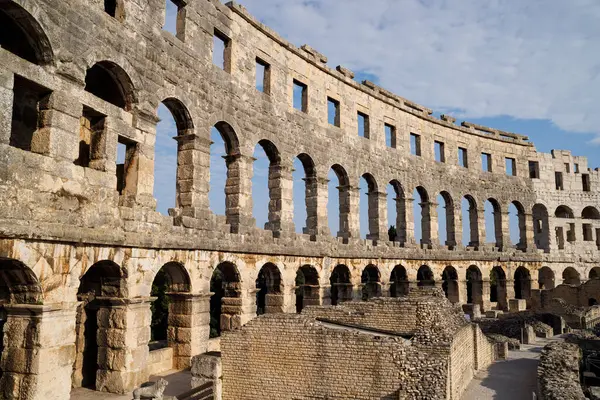 Hırvatistan 'ın Pula kentindeki antik miras. Antik Roma arenasının kemerleri. Tarihi amfi tiyatronun ayrıntıları, mavi arka plandaki yüksek duvarların geniş açılı görüntüsü..