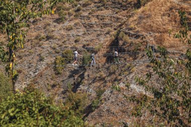 Sasso di Castalda, İtalya - Ağustos 2024: Bir hava manzarası, çevresindeki yeşil ve kahverengi yapraklarla kayalık bir arazide uzanan uzun ve askıya alınmış bir yaya köprüsünü yakalar, maceracı manzarayı ve mühendisliği vurgular..