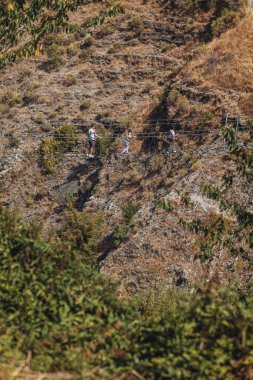 Sasso di Castalda, İtalya - Ağustos 2024: Bir hava manzarası, çevresindeki yeşil ve kahverengi yapraklarla kayalık bir arazide uzanan uzun ve askıya alınmış bir yaya köprüsünü yakalar, maceracı manzarayı ve mühendisliği vurgular..