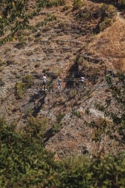 Sasso di Castalda, İtalya - Ağustos 2024: Bir hava manzarası, çevresindeki yeşil ve kahverengi yapraklarla kayalık bir arazide uzanan uzun ve askıya alınmış bir yaya köprüsünü yakalar, maceracı manzarayı ve mühendisliği vurgular..