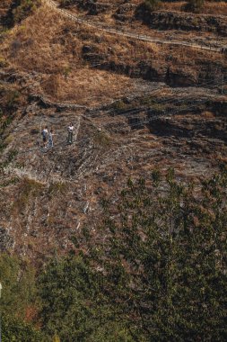 Sasso di Castalda, Italy - August 2024: An aerial view captures a long suspended footbridge   stretching over a rocky terrain with surrounding green and brown foliage, highlighting the adventurous landscape and engineering. clipart