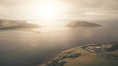 Sun flare at ocean bay reflection aerial. Majestic seascape at mountainous islands at Campbeltown, Scotland, Europe. Bright sunlight at sea coast with green mountain islets. Cinematic soft light shot clipart
