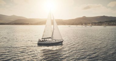 Sun seascape with white sailboat aerial. Mesmerezing landscape with sail boat at summer. Sunlight over sail boat at ocean bay. Sea shore of Arran Island with vessel. Serene water scenery drone shot clipart