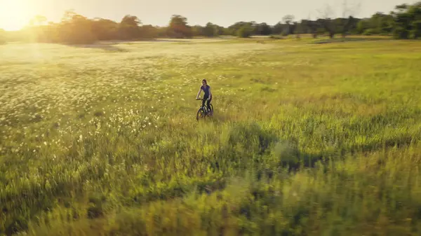 女は太陽の場の空中で自転車に乗る 夏の自然景観 農村部の牧草地で自転車を運転します アクティブなスポーツライフスタイル レクリエーションだ 緑の芝生の谷に咲く花 キエフ市 ウクライナ ヨーロッパ ロイヤリティフリーのストック画像