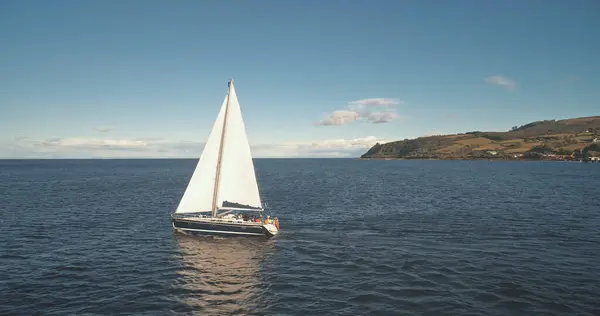 在海港航空的游艇 在豪华游艇上的嘉年华帆船在公海上航行 苏格兰亚兰岛上的布罗迪港夏天的自然海景 电影无人机拍摄 免版税图库照片