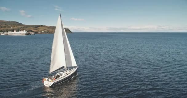 オーシャン湾空中での帆船のゆっくりとした動きを閉じます 海湾でヨットをレースする ブロディック桟橋 アラン島岸 スコットランド ヨーロッパの豪華な帆船のマジェスティックな海岸 シネマティックサマークルーズ ストック映像