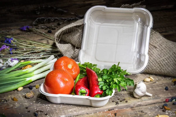 Paprika ve domatesler ahşap bir arka planda çevre dostu tek kullanımlık konteynır içinde.