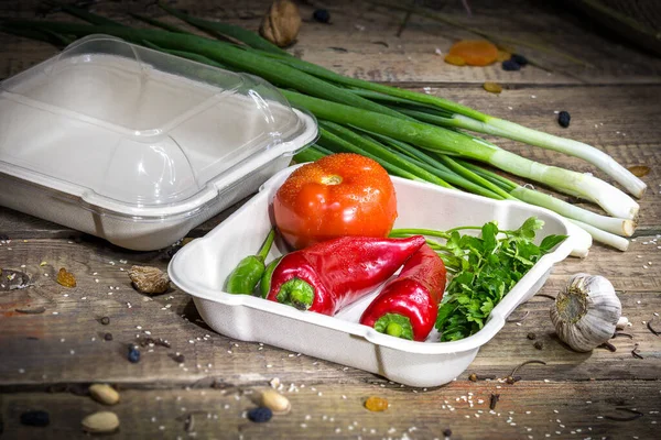 Paprika, domates ve yeşillikler ahşap bir arka planda tek kullanımlık bir kabın içinde.