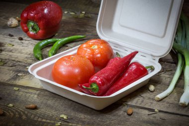 Paprika, domates ve yeşillikler ahşap bir arka planda tek kullanımlık bir kabın içinde.