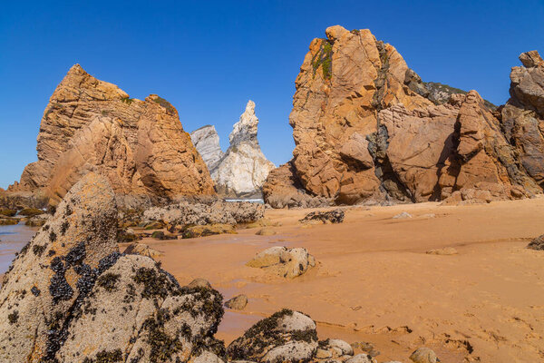 Towering rock cliffs at Praia Da Ursa Beach, Sintra, Portugal. Atlantic ocean waves and sandy beach near famous Cabo da Roca in Portugal