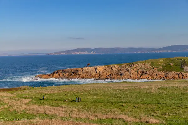 La Coruna, İspanya: A Coruna sahilinde güneşli bir kış gününün tadını çıkaran insanlar, açık mavi bir gökyüzü ve denizin ötesindeki uzak tepeler