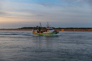 Ilhavo, Portugal: A calm sea as a boat arrives at lhavo port at dusk, with the soft light of late afternoon