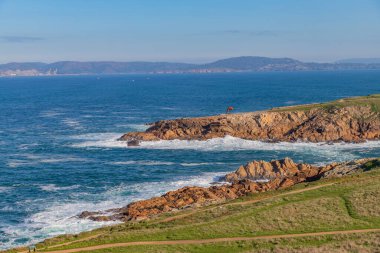 A Coruna 'da kıyı manzarası kayalık uçurumlar, dalgalar onlara çarpıyor ve açık mavi bir gökyüzü.