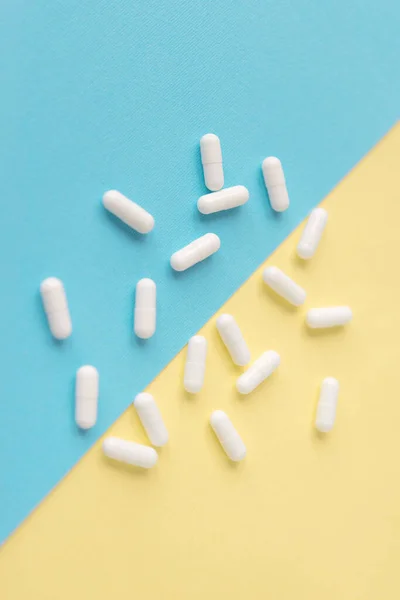 stock image White pills on a yellow and blue pastel background. Capsules pills close-up. health care and medicine.