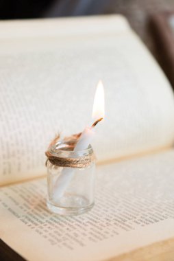 Eski açık bir kitabın arka planında cam bir kavanozda mum yakmak. Arka planda tatil ışıkları yanar.