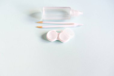 Contact lenses set with saline in bottle, tweezers, plastic case with solution on blue background with copy space