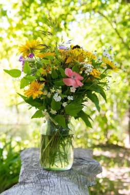 Bir buket parlak, farklı sarı çayır çiçekleri. Basit bir cam kavanozda, doğal bir arka planda.