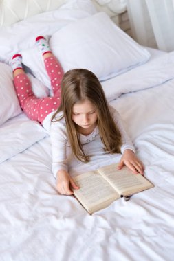 Küçük tatlı kız yatakta kitap okuyor. Masallar. ışık içerisi.