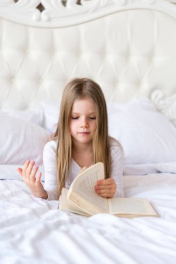 Küçük tatlı kız yatakta kitap okuyor. Masallar. ışık içerisi.