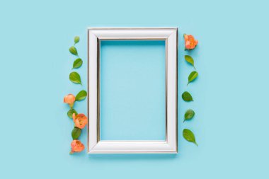 Blank white frame on a plain blue background. poster layout for art display. Top view, copy space. no people. Floral decor. Interior details.