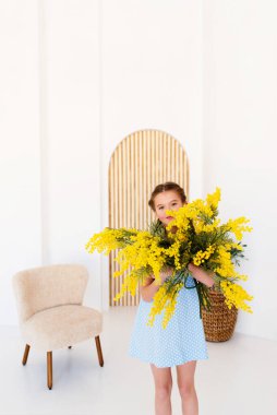 child gives flowers. portrait  little girl with a bouquet of yellow flowers.  girl in a blue dress. Bright interior.