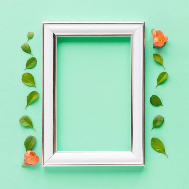 Blank white frame on a plain green background. poster layout for art display. Top view, copy space. no people. Floral decor. Interior details.