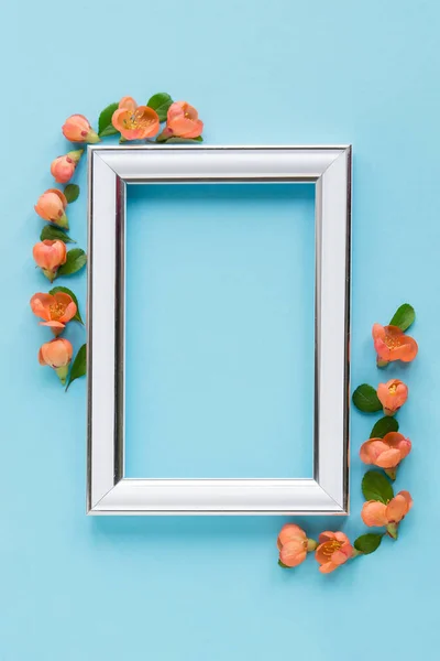 Blank white frame on a plain blue background. poster layout for art display. Top view, copy space. no people. Floral decor. Interior details.